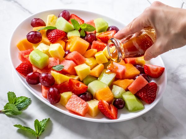 A vibrant bowl of fruit salad topped with white peony honey syrup