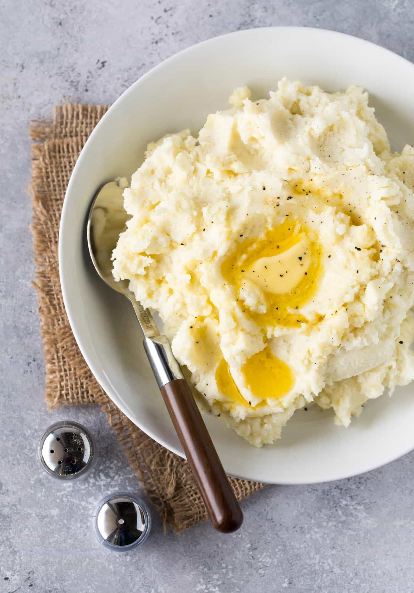 White bowl filled with mashed potatoes with melted butter on top. Small