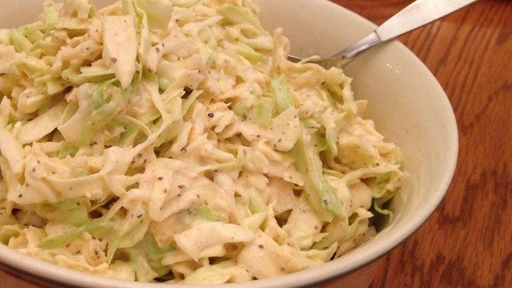 A bowl filled with coleslaw on a wooden table next to a fork