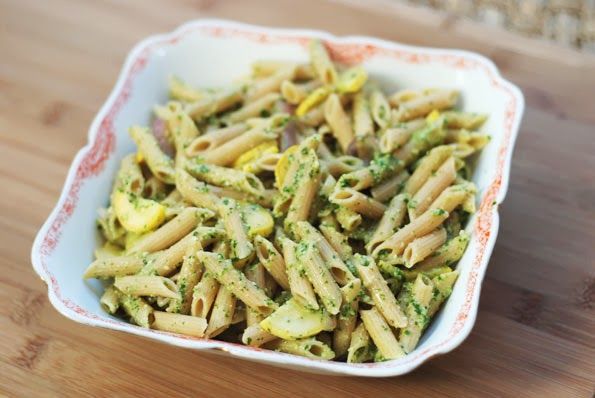 A bowl of vibrant green herb pesto with fresh herbs around it