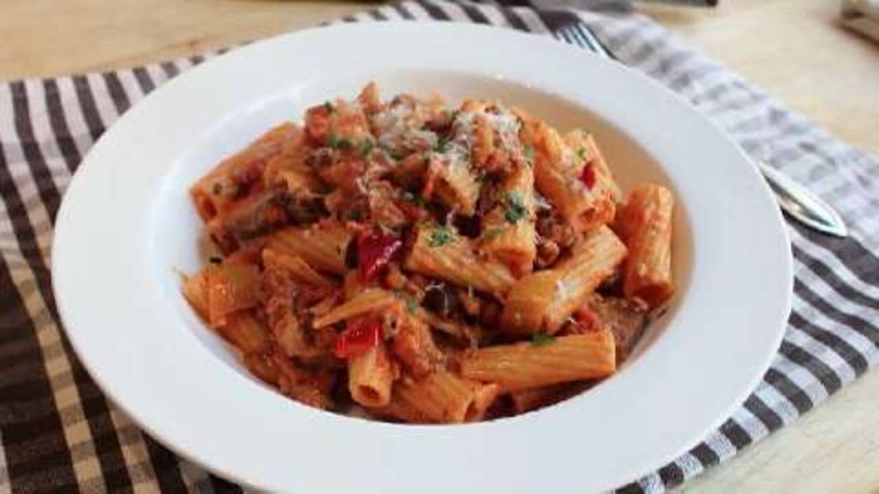 a white plate topped with pasta and meat next to a fork, knife and spoon