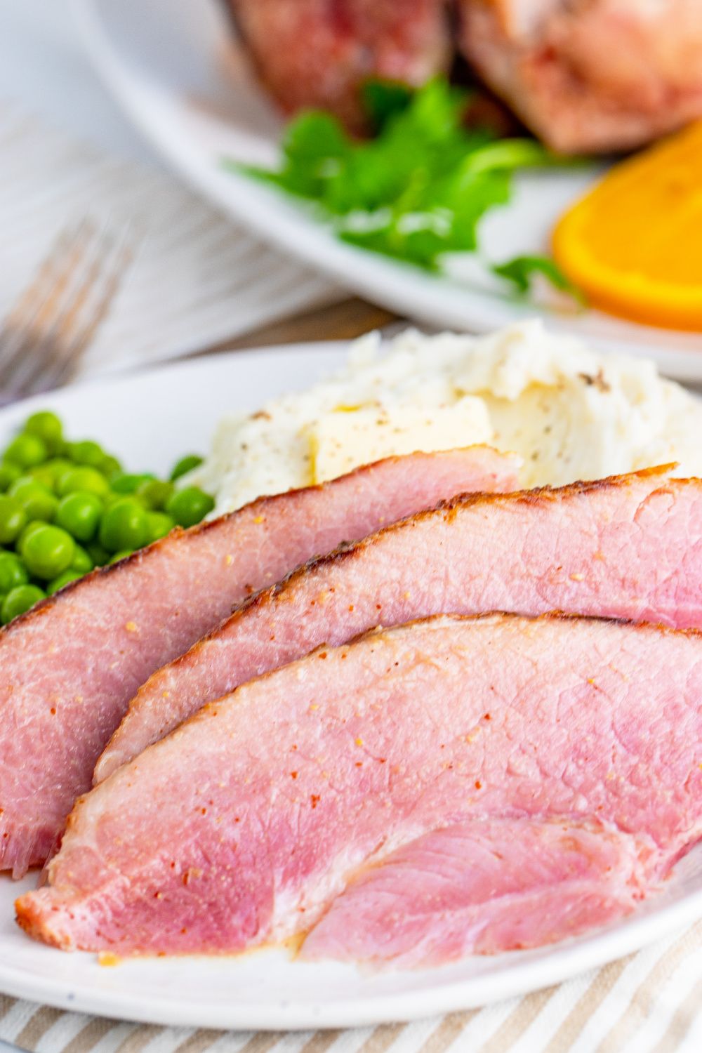 A white serving plate full of ham slices, mashed potatoes and peas