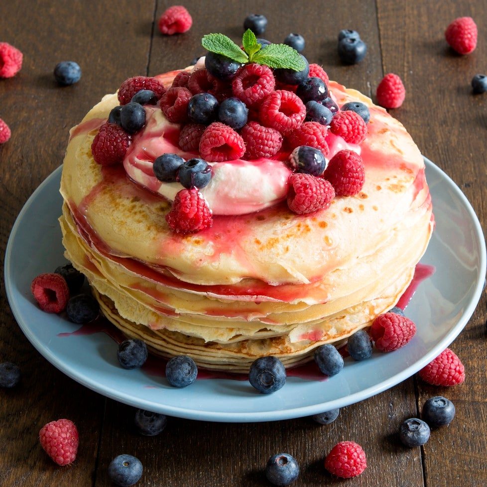 A stack of mixed berry pancakes topped with whipped cream and fresh berries