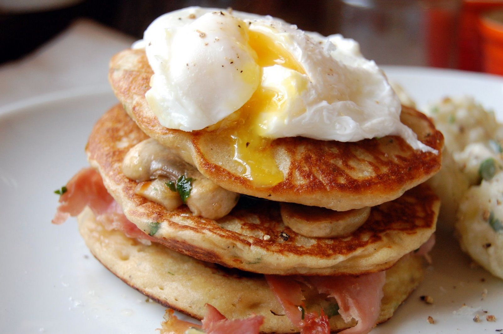 A stack of pancakes with eggs on top and some other food items next to it