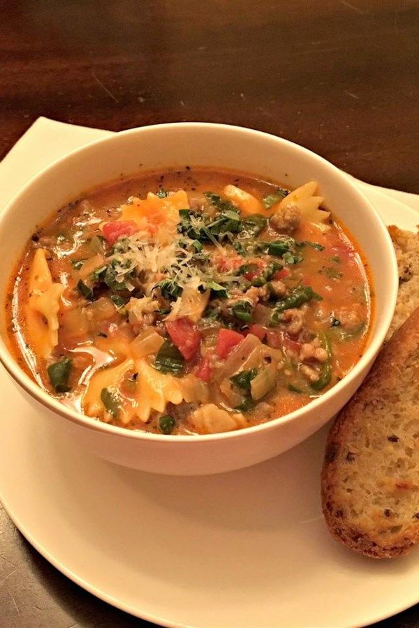 A white plate topped with a bowl of soup next to a slice of bread